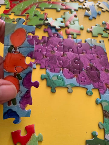 fingers holding brightly colored interlinked puzzle pieces with other pieces in the background (Photo Credit to Cary Pasqualle