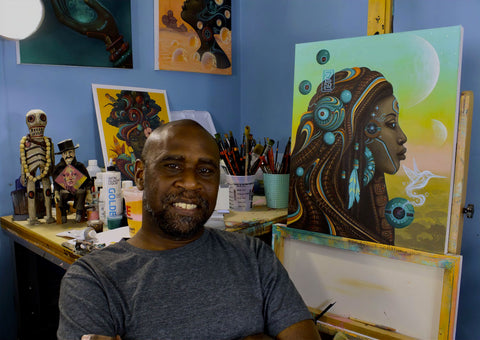 Paul Lewin smiling into the camera, sitting in front of several paintings
