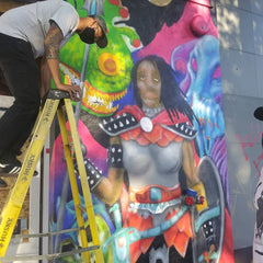 Person with a face mask and cap climbing down from a ladder in front of a mural