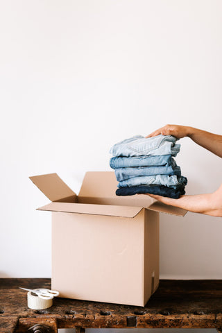 Cropped person packing jeans into carton container during a spring closet cleaning to store them for the season