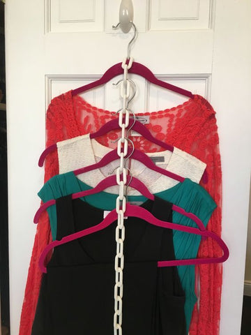 A white chain has red hangers stacked through every few links on a hook on the back of the store as inspiration for hanger storage in small spaces