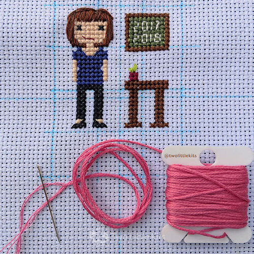 A photo of a work-in-progress cross-stitch piece with a wound-up bobbin of pink DMC floss