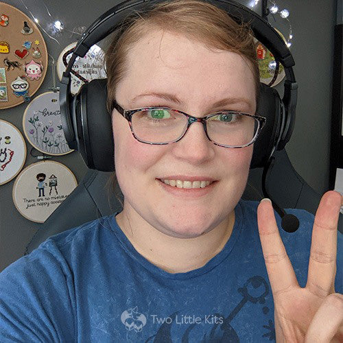 A photo of Kate showing a "peace" finger sign wearing large headphones before the recording of the podcast itself