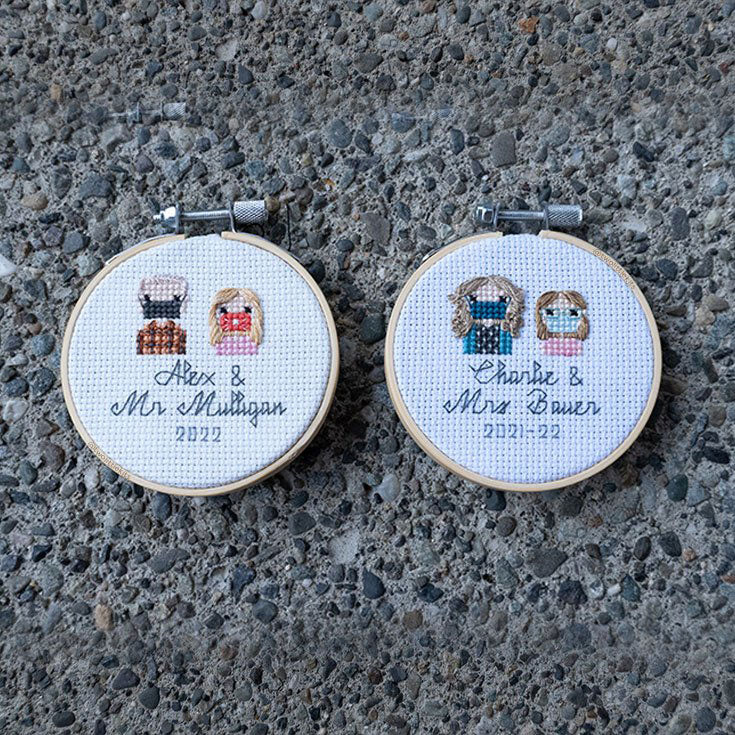 Two 3in embroidery hoops of crosss-stitched pieces that all include one [different] adult and one [different] little girl on both as bust shots. They are stitch people portraits and all say the child's name and then their teacher's name with the date '2021-22' underneath. They are all laid flat on a stony floor.