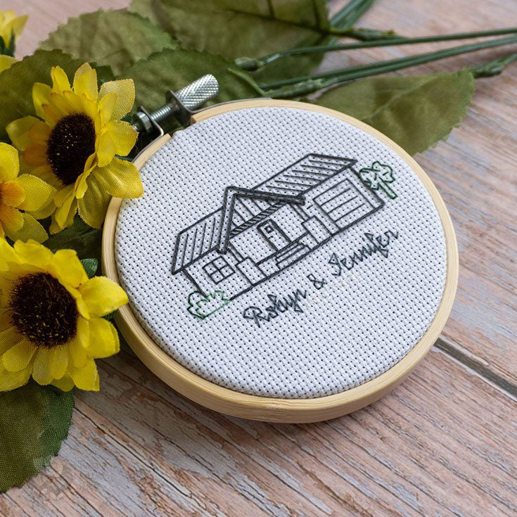 A small backstitched piece of a house outline with bushes that reads 'Robyn &amp; Jennifer' underneath it.