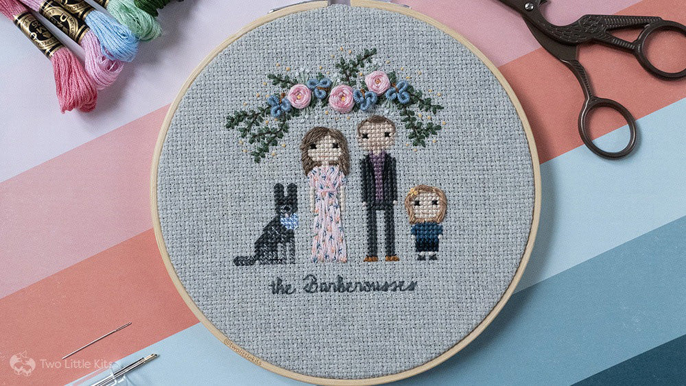 A cross-stitch and hand embroidered stitch people family of a man, woman and young son. Around them is text and embroidered flowers.