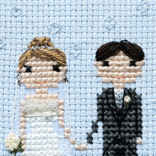 A photo of a cross-stitched bride and groom holding hands.'