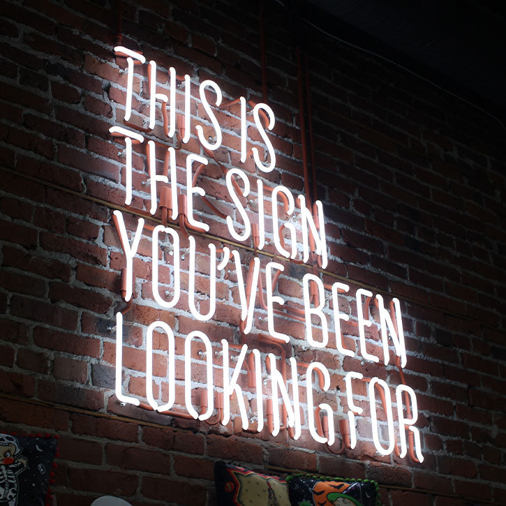 A large neon sign on a brick wall. The sign reads "THIS IS THE SIGN YOU'VE BEEN LOOKING FOR"