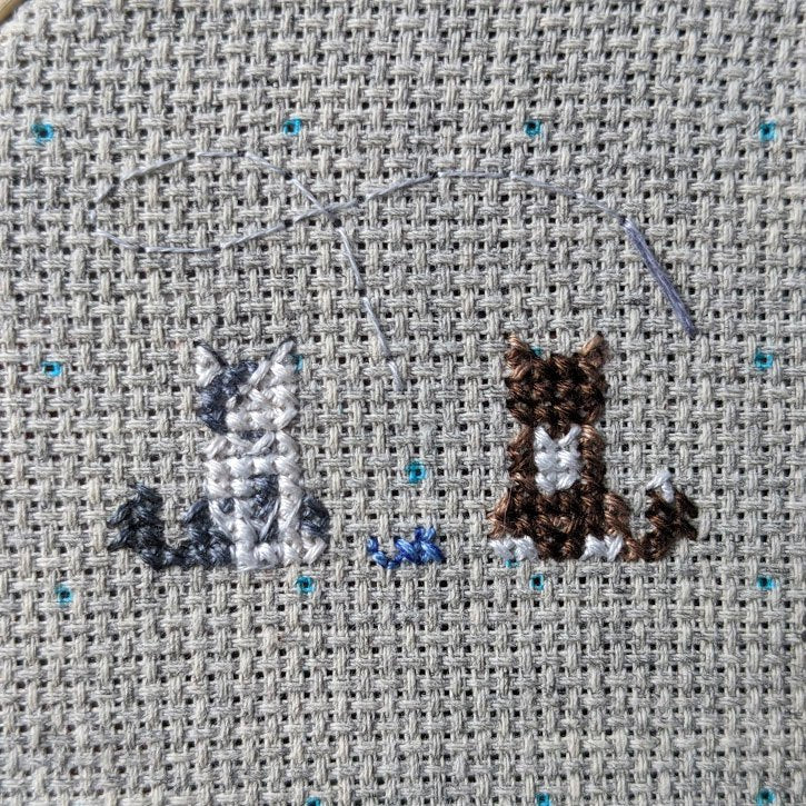 Two cross-stitched cats - one white & grey, the other is white and dark brown.