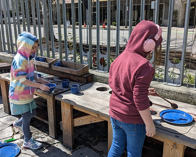 Two young girls playing outside together at a pretend kitchen