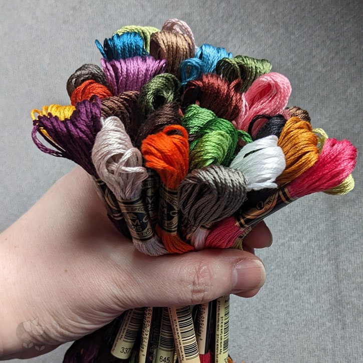 A hand grabbing onto a colourful bundle of DMC embroidery floss.