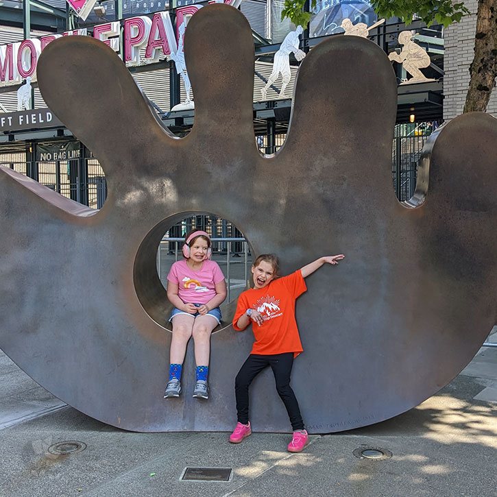 Two young girls posing in front of a large statue of a baseball mitt.