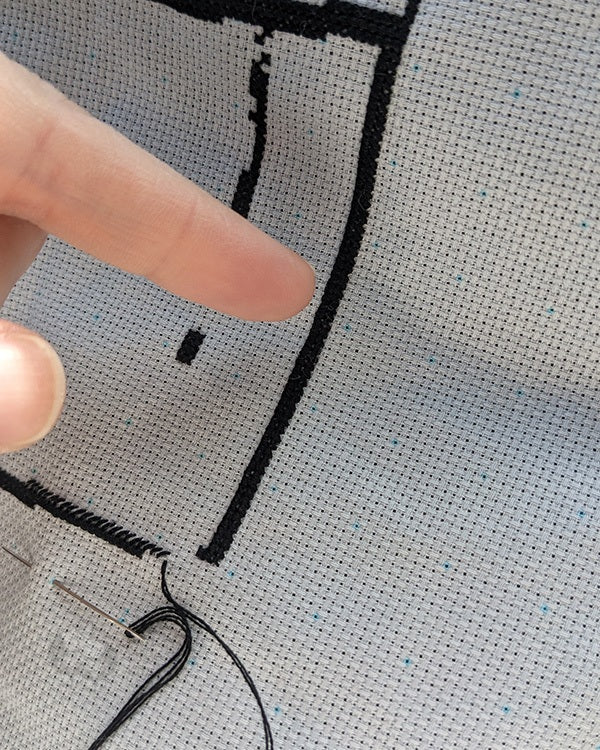 A hand pointing to a column of black cross-stitches