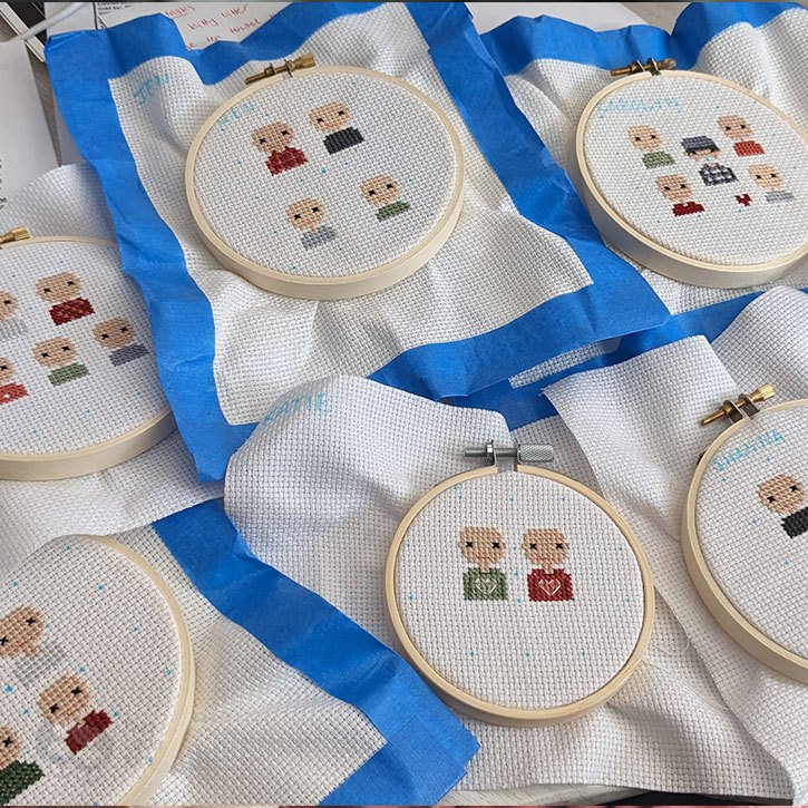 A mesh of cross-stitched holiday ornaments as works-in-progress. Some of them are outlined in blue painters tape.