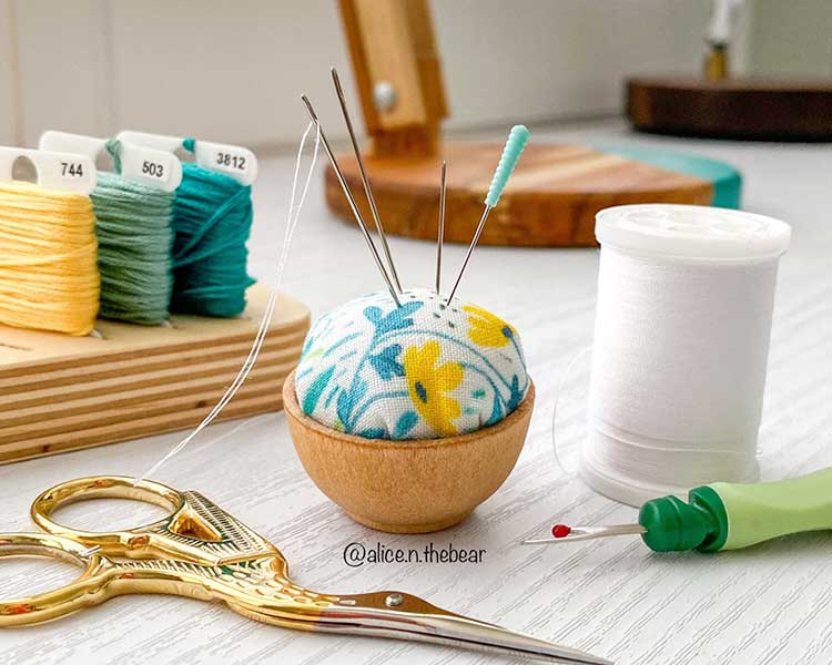 An adorable pin cushion with other sewing notions around it.
