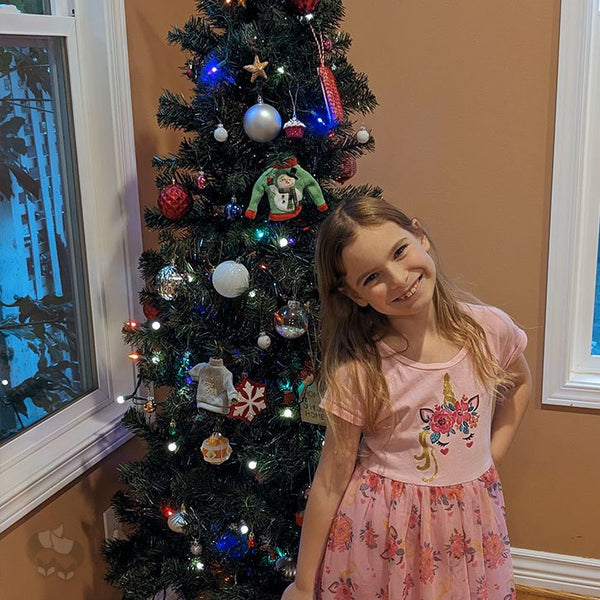 A Christmas tree and a young girl standing in front of it, smiling.