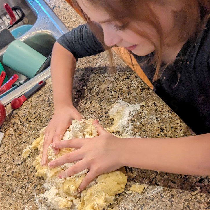 A little girl enthusiastically kneading cookie dough.