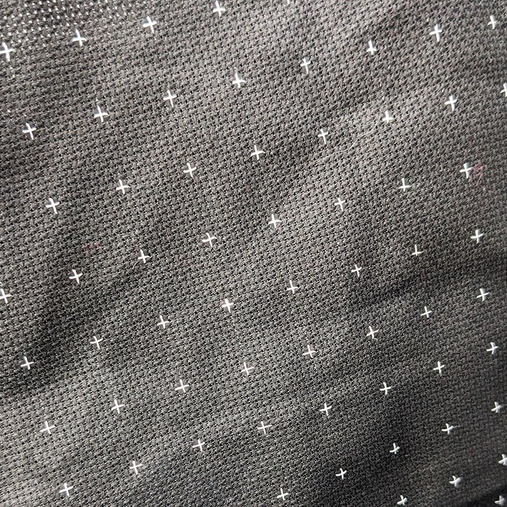 A photo of black Aida fabric with lots of tiny white crosses on it in a 10x10 grid.