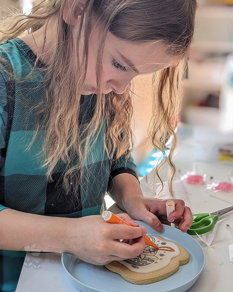 A young girl concentrating on colouring a cookie with special edible-ink markers.