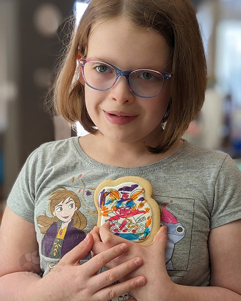 A young, special-needs girl with a soft smile holding her cookie that has colourful, edible ink scribbled on it.