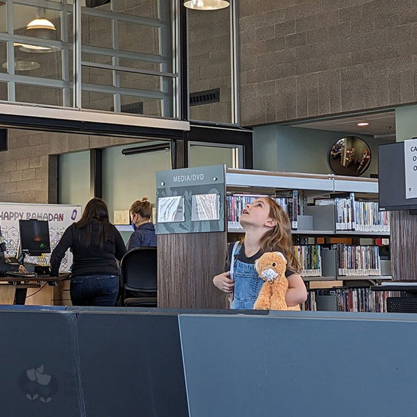 A little girl looking up at a water feature in a local library. She is cradling an orange stuffy.
