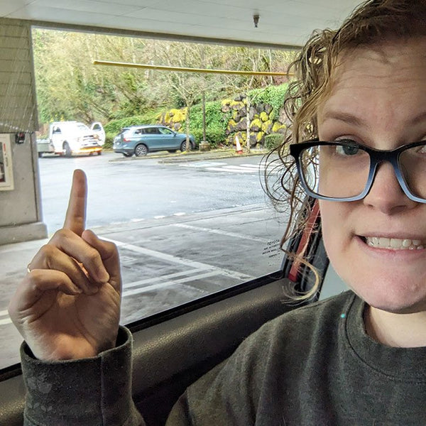 Kate, sitting in her car, pointing to a car mechanic.