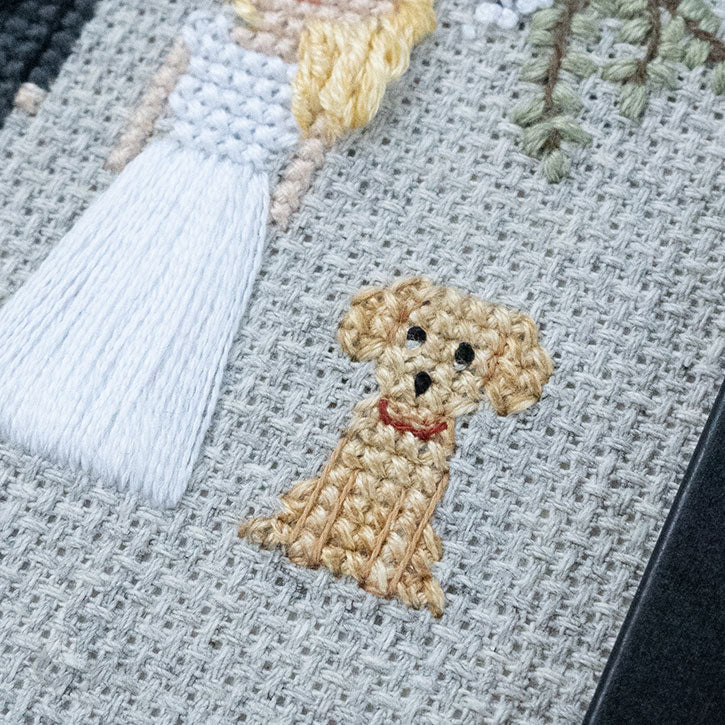 A cross-stitch piece depicting a sitting dog. The photo is up-close to the piece itself.