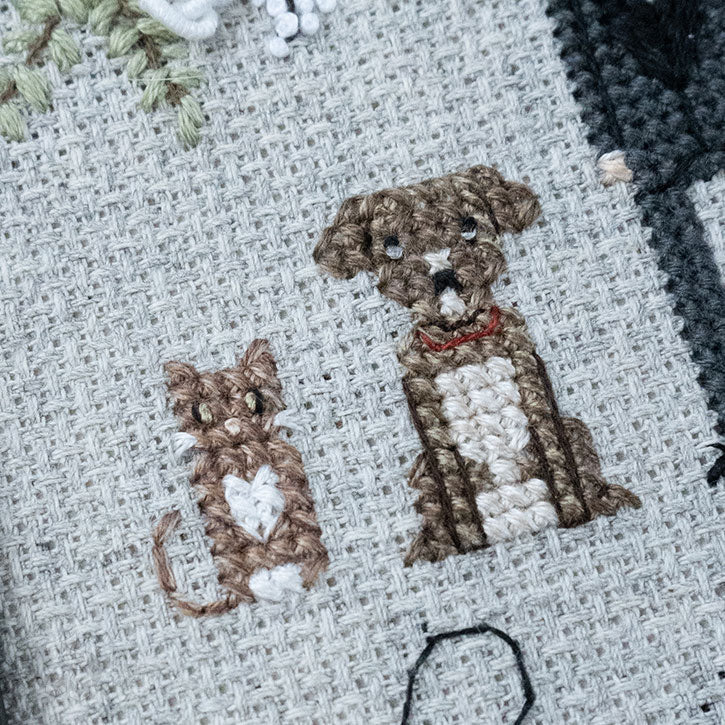 A cross-stitch piece depicting a sitting cat and a sitting dog. The photo is up-close to the piece itself.