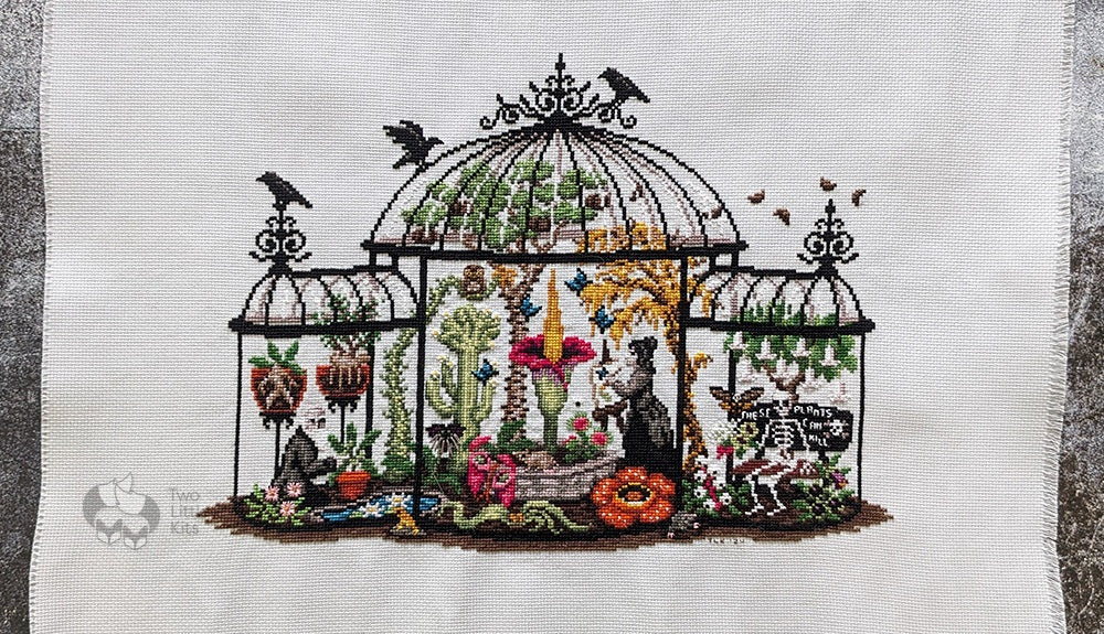 A large cross-stitched finished piece called "Greenhouse of Oddities" by Lola Crow. It's stitched on 18ct Aida fabric and is extremely detailed.
