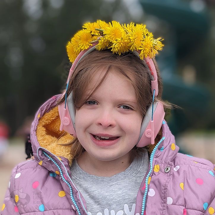 A sweet 9-yo girl smiling, wearing a puffy coat and a handmade, real daisy-chain flower crown on her head.