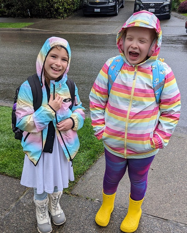 Two young, happy girls standing outside in the wet waiting for the bus.