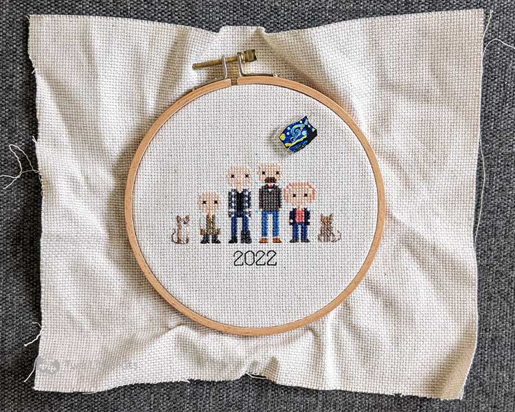 A work-in-progress cross-stitch of a stitch people family with 4 people and 3 cats