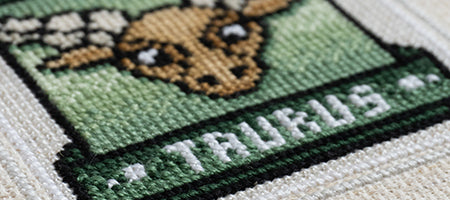 A close-up photograph of a cross-stitch pattern called "Zodiac: Taurus". The pattern depicts a zodiac ox on a green-gradient background.