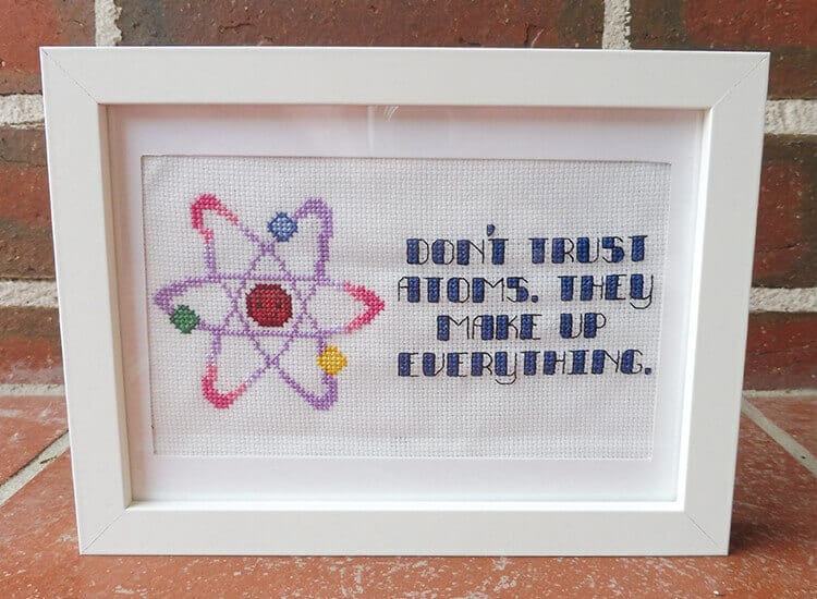 A cross-stitch of a colourful atom and a funny pun with it.