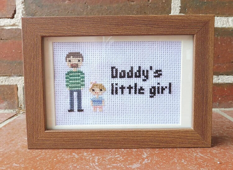 A framed cross-stitch portrait of a dad and young daughter.