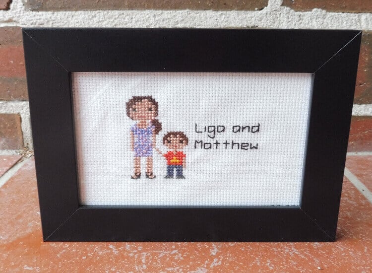 A cross-stitch portrait of a mum and son in a black frame.