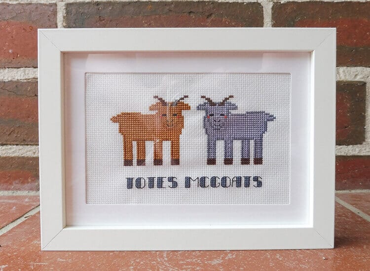A framed cross-stitch of two goats and the words "Totes Magotes"