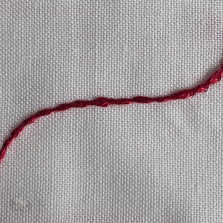 A curved, red line of embroidery floss, demonstrating a stem stitch