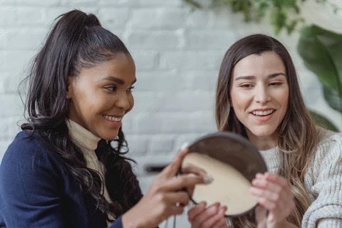 imagem de duas mulheres e uma delas olhando-se no espelho, satisfeita com o resultado de um tratamento de beleza