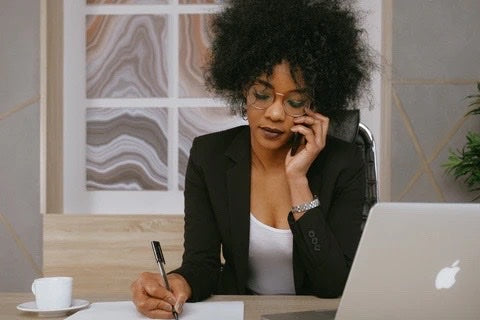 mulher sentada em frente ao computador fazendo anotações em escritório de trabalho