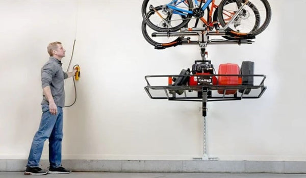 Man Operating A Wall Mounted Control To Adjust The Top Shelf Storage The Storage Lift That Is Suspending Bicycles And Storage Bins High Up On A Garage Wall