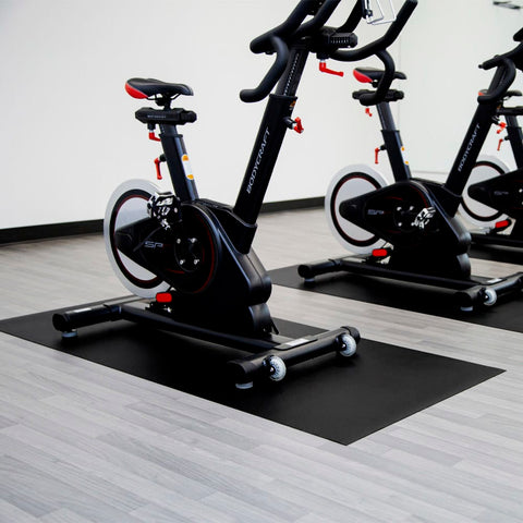 Stationary Exercise Bikes With Black Frames Positioned On Dark Equipment Mats With Light Colored Flooring