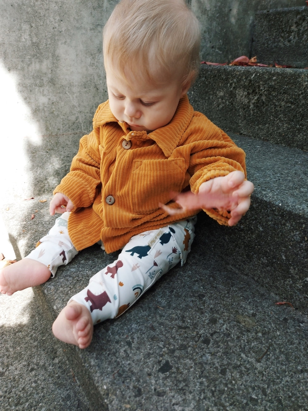Junge trägt einen Teil seiner Capsule Wardrobe. Eine Hose aus Biojersey mit Dinos und eine Übergangsjacke aus Cordnicky