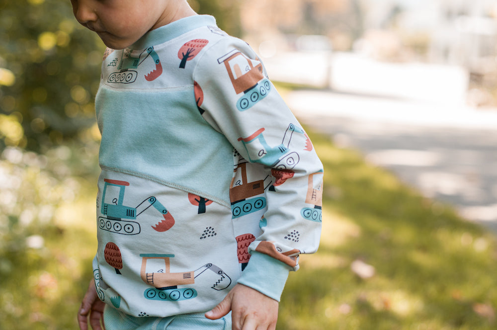 Ein Junge seitlich fotografiert. Er trägt einen Pullover mit Baggern und Herbstbäumen aus Biojersey.