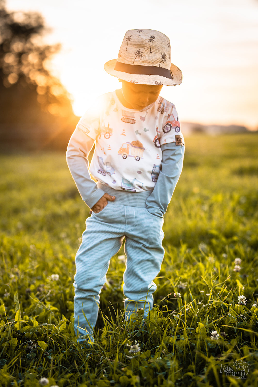 Kleiner Junge steht auf einer Wiese im Sonnenuntergang. Er trägt selbstgenähte Kleidung aus Biostoffen von Faybee