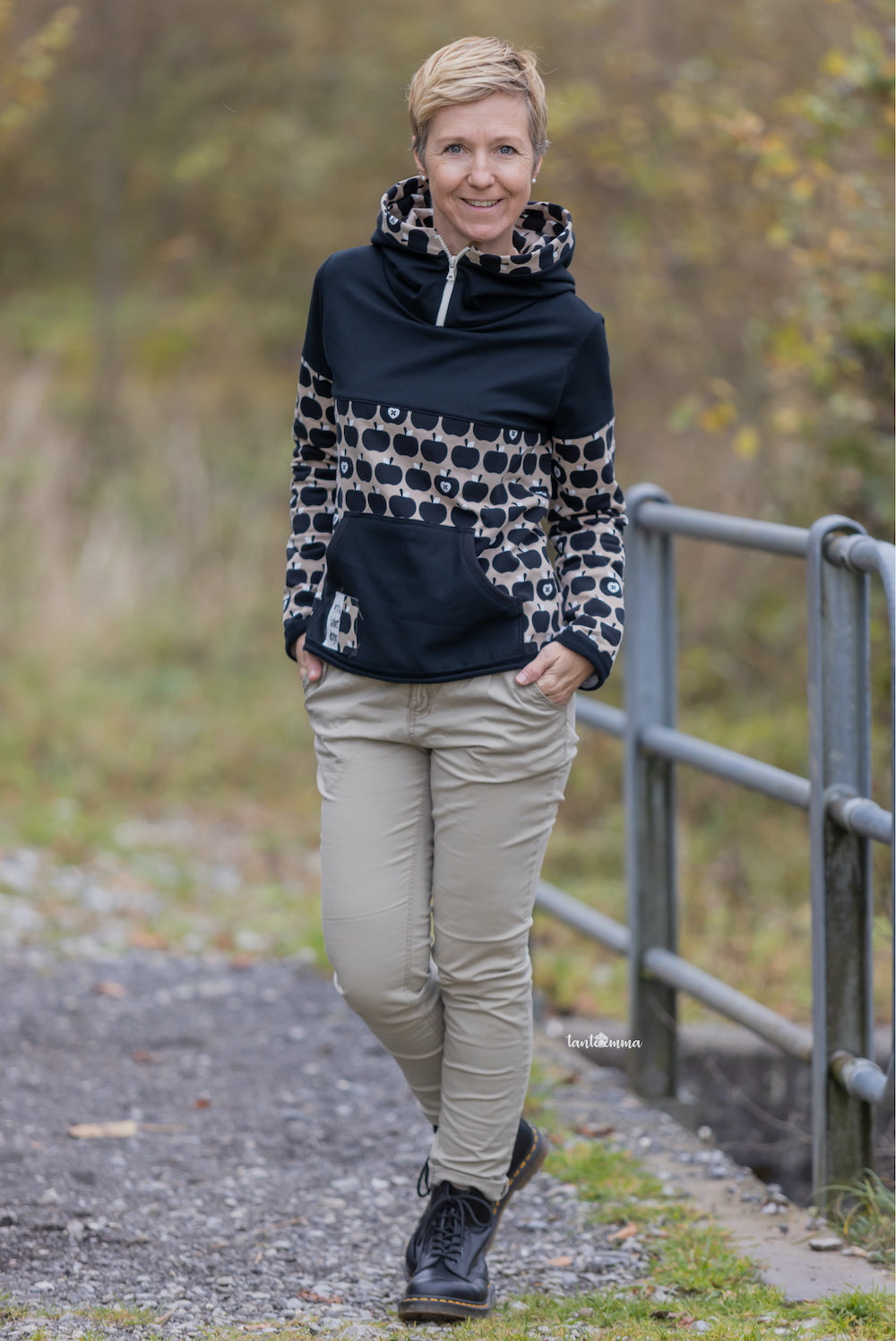 Frau steht im Freien. Sie trägt einen selbstgenähten Hoodie mit sportlicher Teilung und Reissverschluss am Kragen. Stoffe sind von fayee.ch