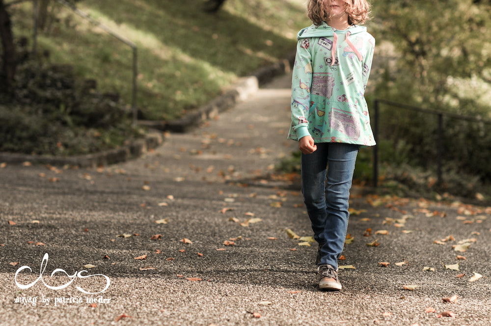 Mädchen mit Hoodie läuft auf einer herbstlichen Strasse. Alles zu Schnittmuster und Stoff erfährst Du in diesem Blogartikel bei faybee.ch