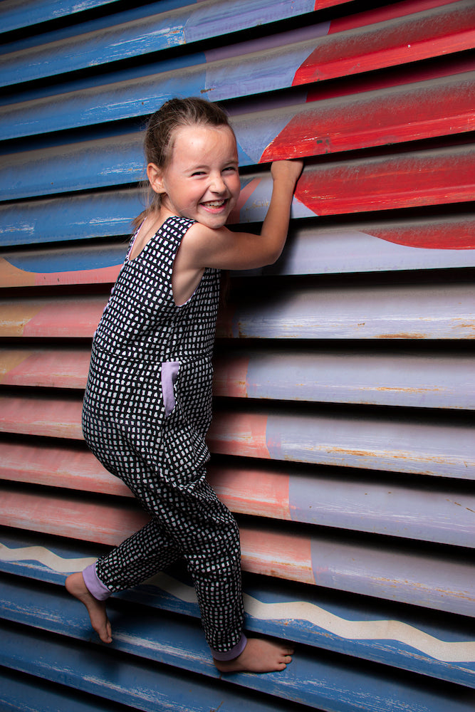 Mädchen klettert an bunter Wand in Overall aus Faybee Biojersey