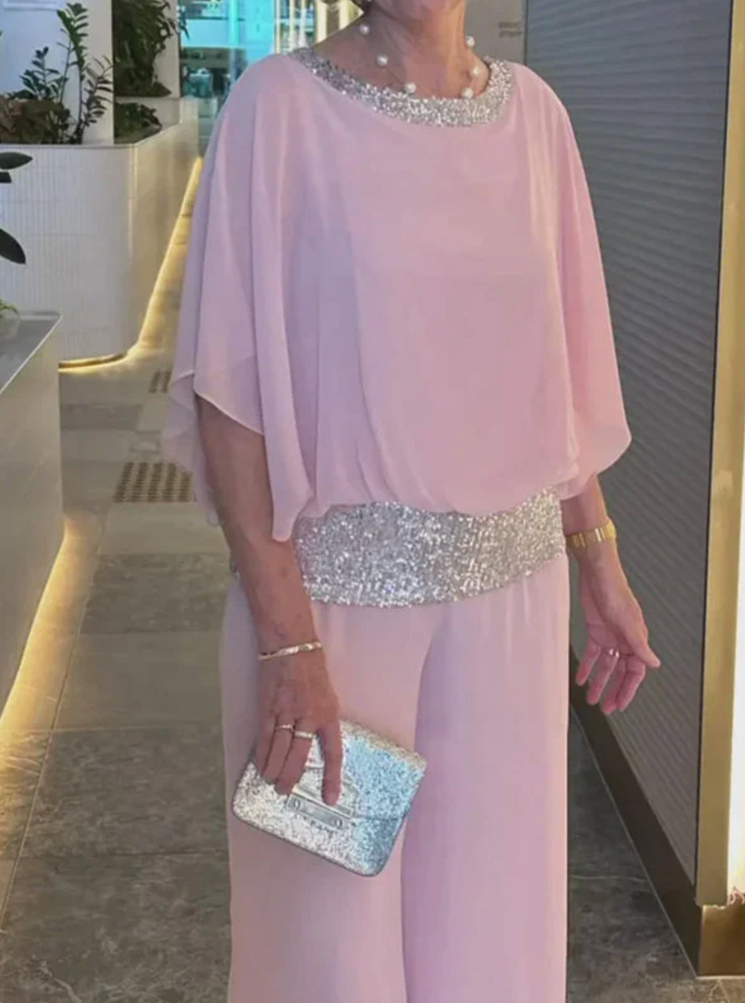 Woman wearing elegant white evening ensemble with sequin details at neckline and waist, holding silver clutch