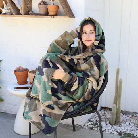 An energetic girl in a camouflage hooded blanket sitting in the backyard